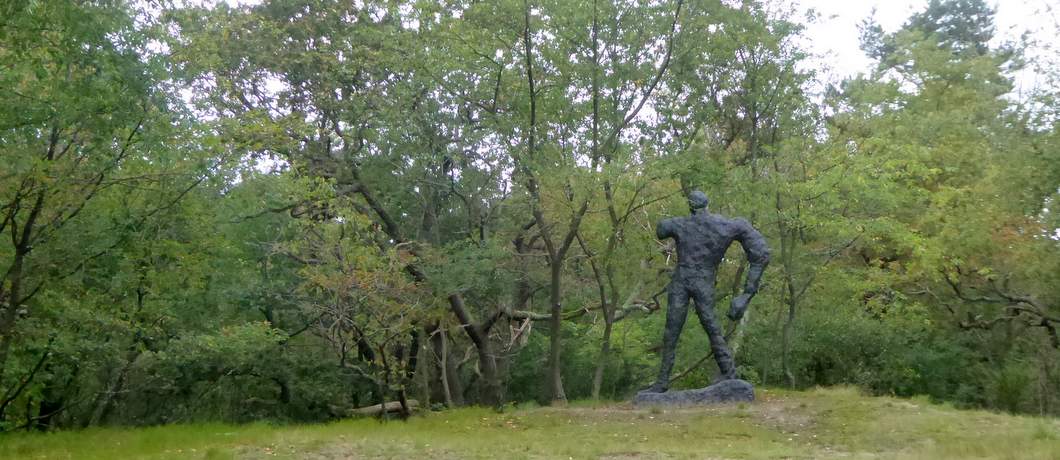 De grote tweedimensionale bronzen man Das Gestalt van Armando bovenop het duin in beeldentuin Clingenbosch