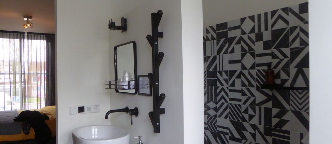 Zwart-wit badkamer met inloopdouche Kamer met open badkamer Oog voor detail zoals flessen en klerenhangers bij B&B Stadsslaperij Tilburg