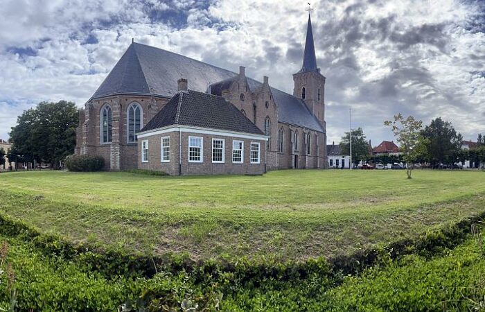 De Sint-Adriaanskerk van ringdorp Dreischor met eromheen de Ring met gras, een gracht en monumentale panden.