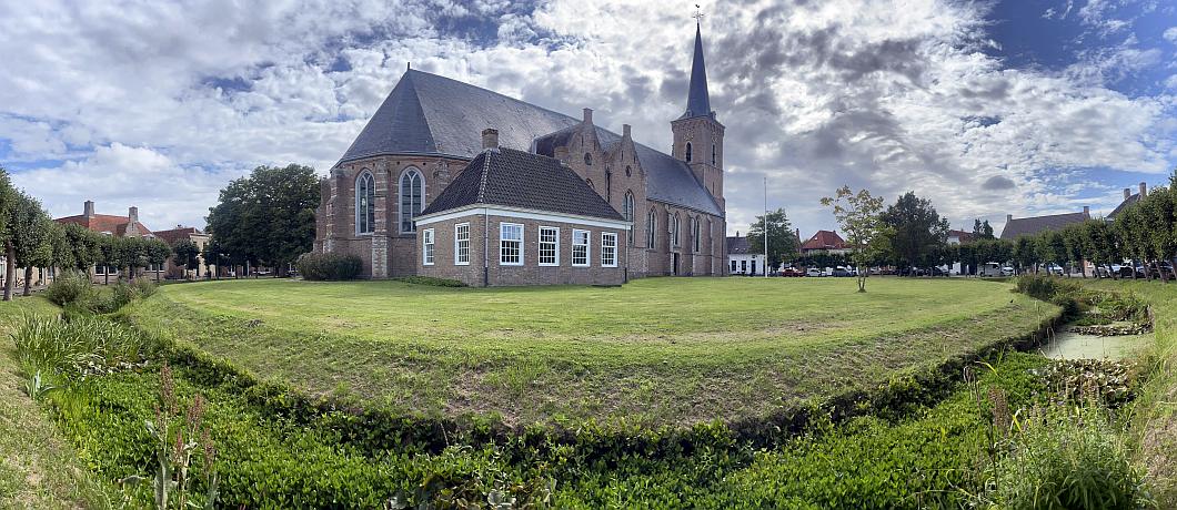 De Sint-Adriaanskerk van ringdorp Dreischor met eromheen de Ring met gras, een gracht en monumentale panden.